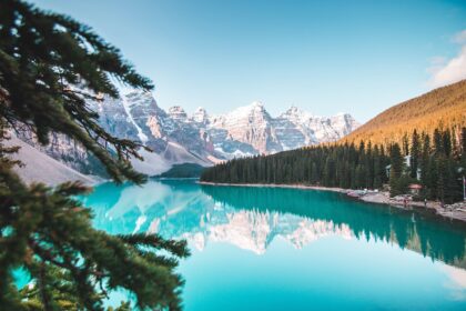 Photograph of a blue lake in Canada with trees and snowy mountains in the background